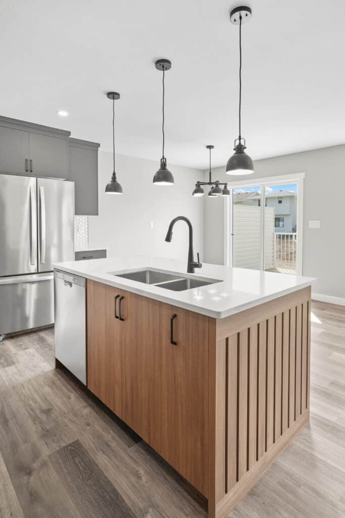 Cuisine Moderne Îlot Bois Luminaires Design Acier Cuisine moderne avec îlot central bois et comptoir blanc, éclairage suspendu noir, électroménagers acier inoxydable et porte-patio.