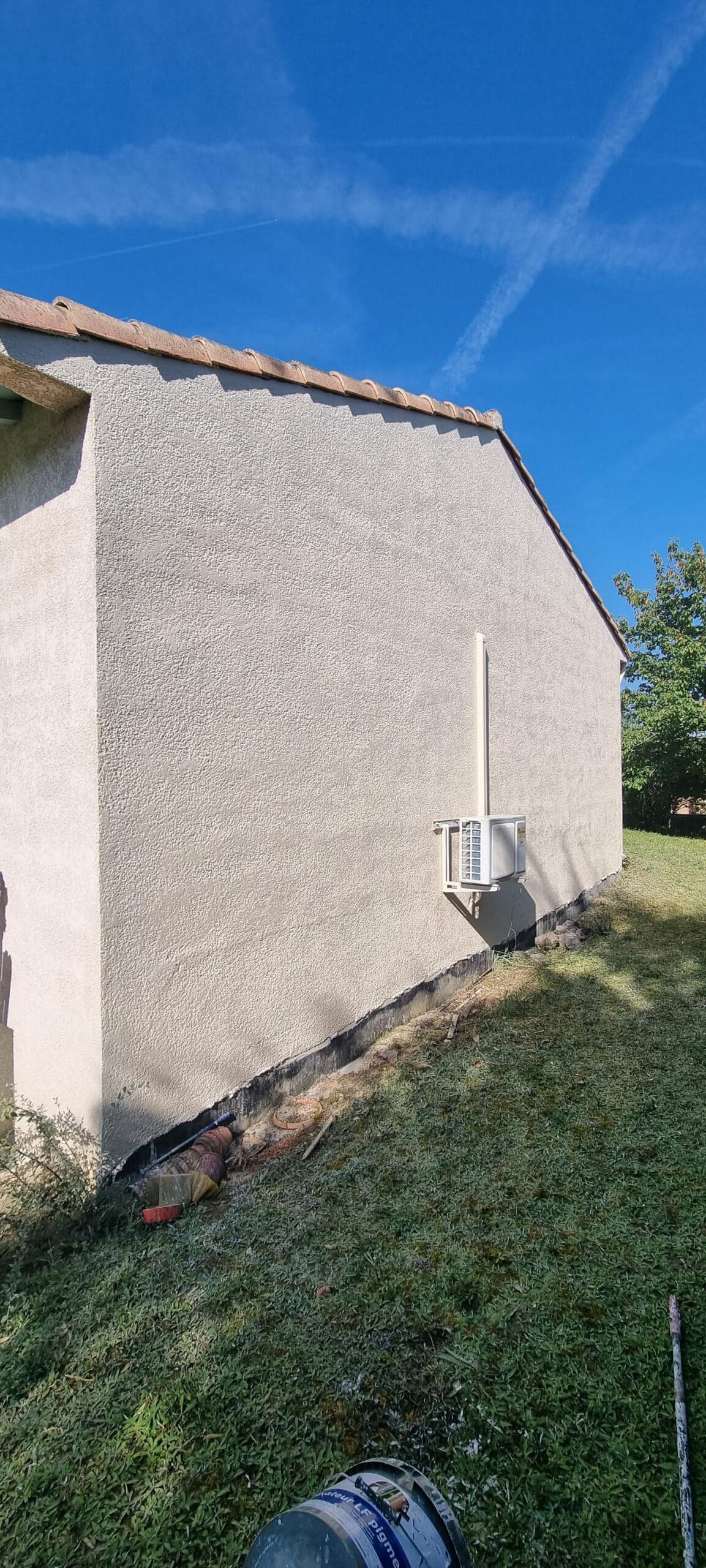 Climatisation installée sur façade en crépi avec un pot de fixateur LF pigmenté visible, sous un ciel bleu.