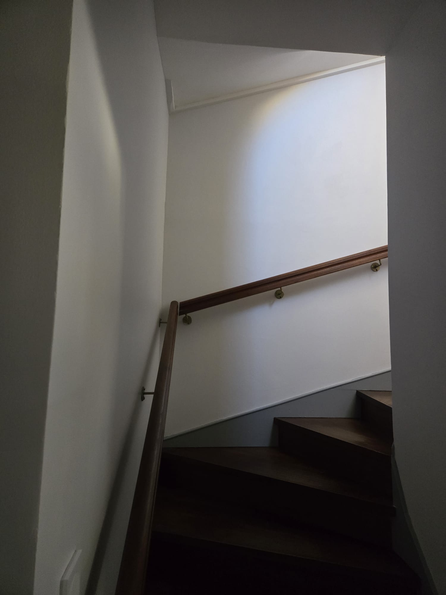 Escalier tournant en bois avec rampe assortie et murs blancs minimalistes sous une lumière douce.