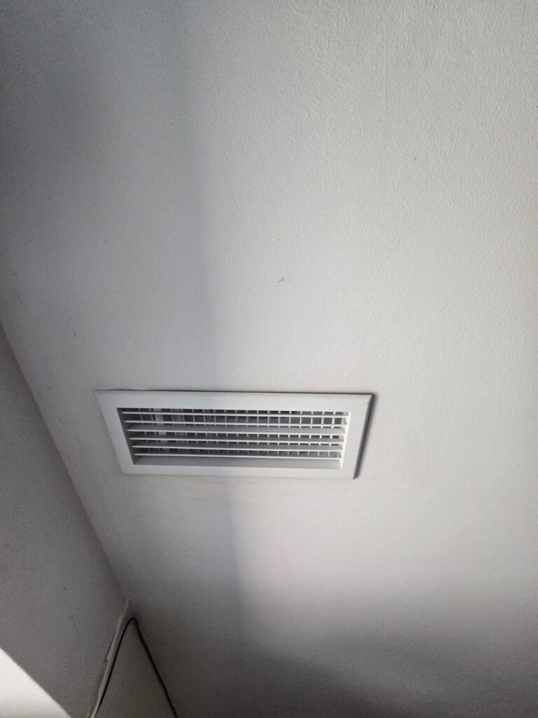 Bouche d'aération rectangulaire blanche pour intérieur Bouche d'aération rectangulaire blanche à lamelles horizontales encastrée dans un plafond blanc épuré.