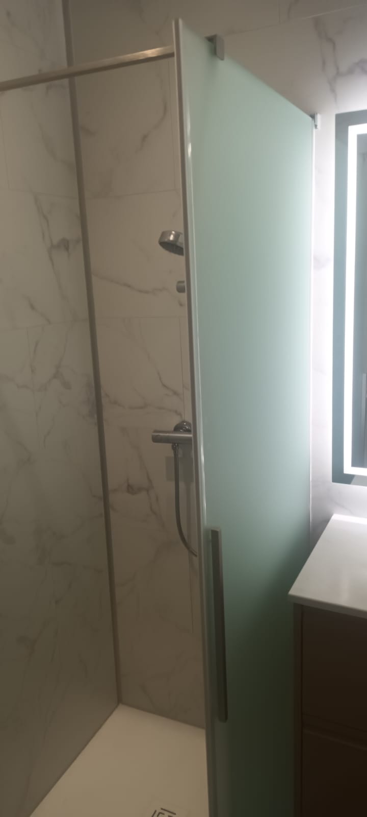Paroi de douche en verre dépoli dans une salle de bain moderne avec carrelage imitation marbre et robinetterie.